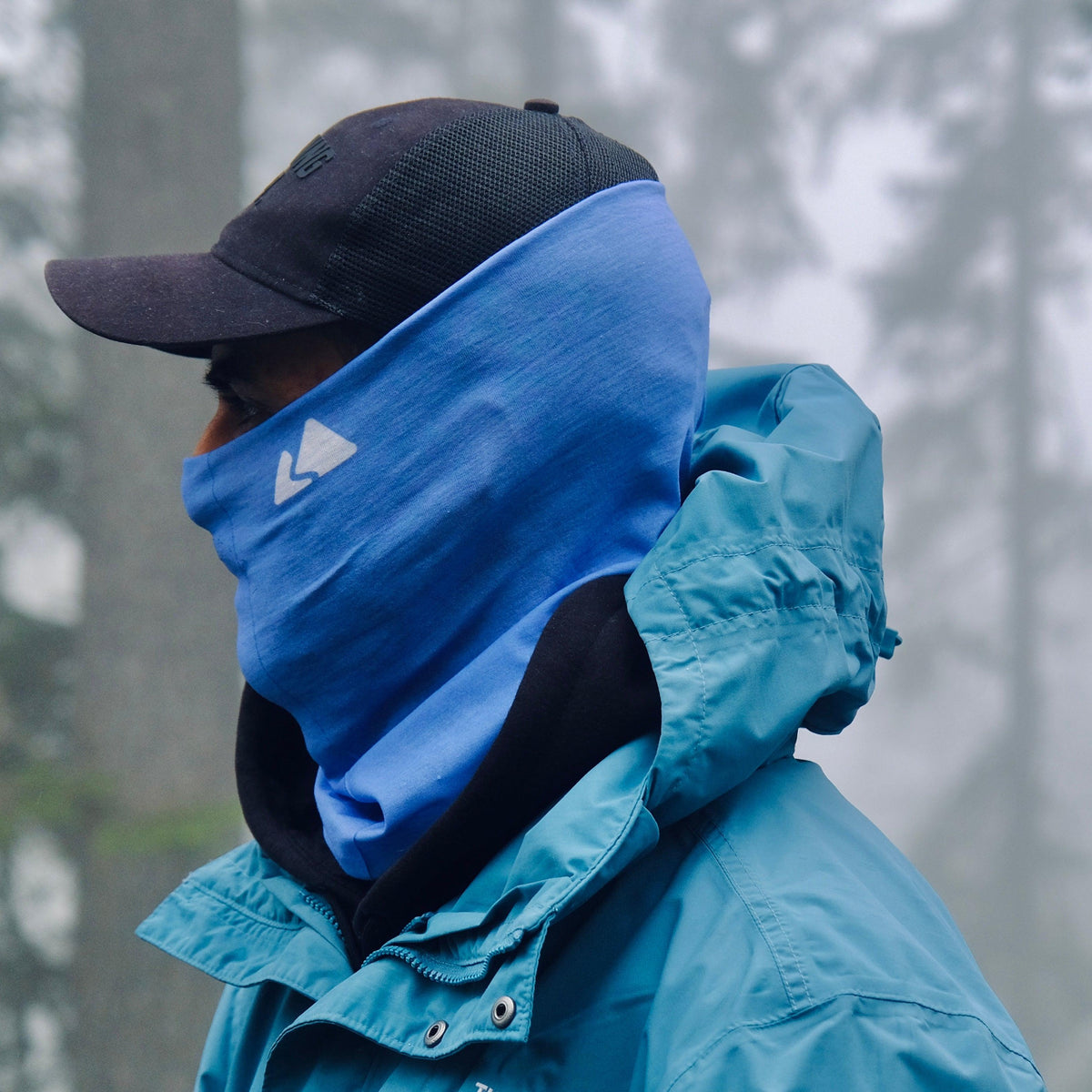 Neck warmer gaiter displayed on a male model. With a white mountain logo. Day Sky Blue colour. 